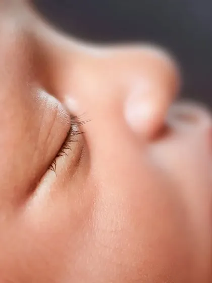 A detailed shot of a newborn's closed eye, highlighting their delicate, long eyelashes.