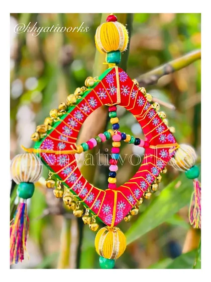 The kite hanging shining in the natural light. The vibrant red and green threads, along with the golden ghungroos, create a truly festive look.