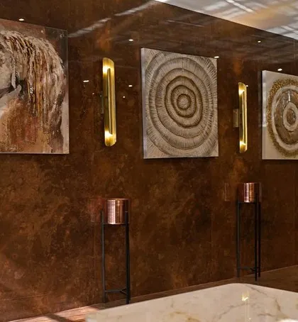 A detail of the art wall in the hotel lobby. The textured wall finish provides a rich backdrop for a curated selection of abstract and figurative art, illuminated by sleek, modern wall sconces to create a moody and luxurious atmosphere.