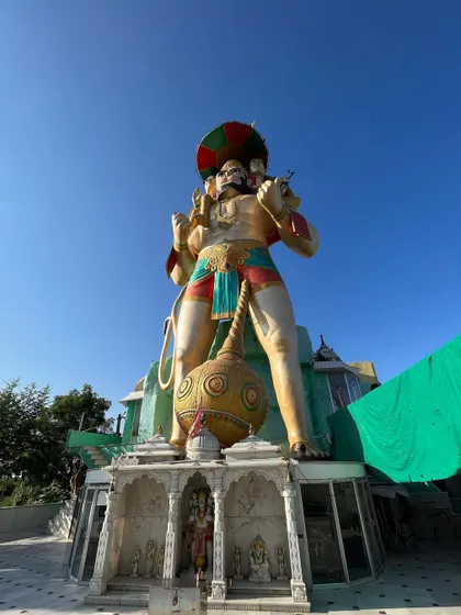 A frontal view of the giant Hanuman statue, showing the small shrine at its base.