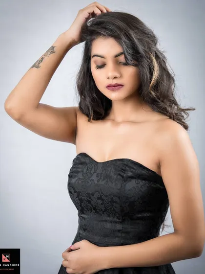 A moody portrait from the 'Unapologetic' series. The model, in a black strapless dress, looks down with a thoughtful expression, her pose conveying quiet strength.