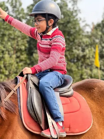 Waving from horseback, this young rider is clearly enjoying his session. We celebrate the enthusiasm and progress of every student.