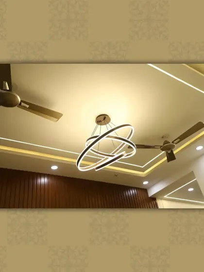 This ceiling combines linear strip lighting with a modern, multi-ring chandelier, offering both ambient and decorative illumination.