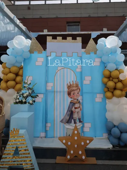 A charming photo spot within the prince-themed party, featuring a blue castle wall, a cutout of a little prince, and balloon accents.