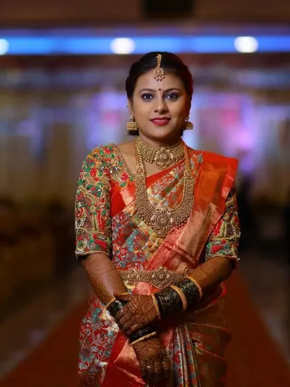 This bride is ready for her ceremony. The hand-embroidered blouse, rich with green, red, and gold threadwork, makes a stunning statement against her printed silk saree.