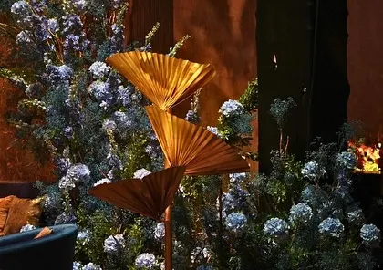 A unique floral arrangement incorporating large, golden paper fans, blending textures and materials.