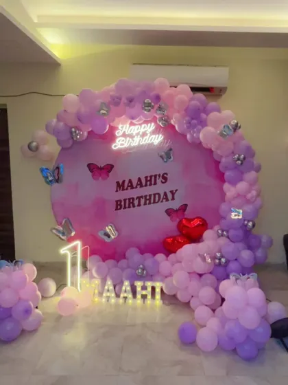 The butterfly theme decoration for 'Maahi's' birthday, shown here without the blue focus lights. The pink and purple color scheme creates a soft and dreamy atmosphere.