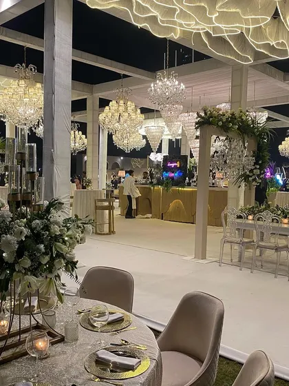 A breathtaking reception design featuring a unique ceiling installation of sculpted white fabric that glows from within. This is complemented by a forest of crystal chandeliers of varying sizes, creating a truly magical, cloud-like effect.