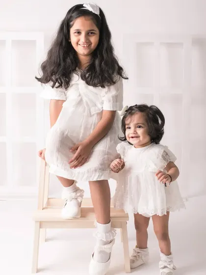 A proud big sister stands by her little sister. The height difference and their sweet interaction make this a charming portrait.