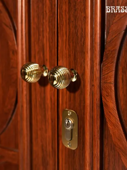 A close-up of the Beehive knobs on the carved wooden cabinet doors, showcasing their intricate design and warm polished brass finish.