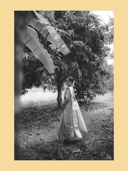 A serene black and white portrait of the bride in a grove. The framing through the leaves adds a sense of intimacy and artistry to this pre-ceremony moment.