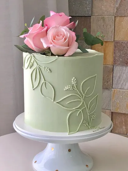 A simple and elegant sage green cake. The design features delicate leaf piping and is topped with fresh pink roses for a natural and beautiful look.