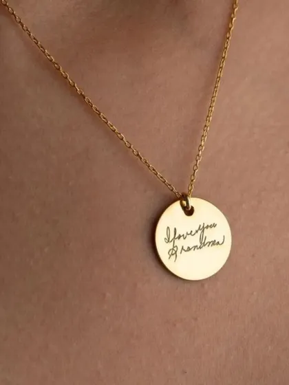 Turn a cherished memory into a timeless keepsake. This round gold pendant is engraved with a loved one's actual handwriting, "I love you grandma", creating a uniquely personal and sentimental piece of jewelry.