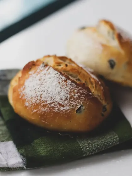 A pair of olive bread rolls on a checkered napkin, showcasing a simple but elegant presentation.