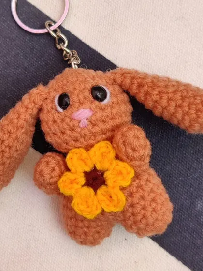 A brown bunny keychain holding a sunflower.