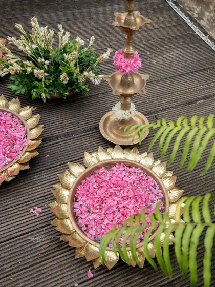 Elegant decor details, including brass urlis filled with pink petals and traditional lamps, set against a wooden deck.