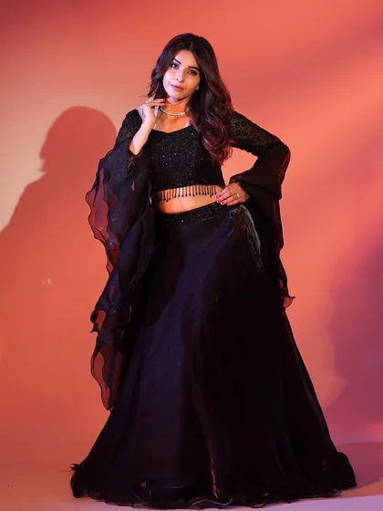 A full-length shot of the black lehenga against a dramatic background. The flowing fabric and bell sleeves create a powerful and elegant silhouette.