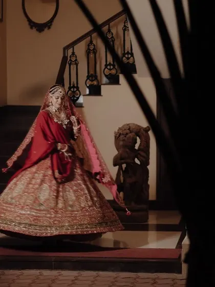 A bride in a traditional red lehenga, captured mid-twirl on a staircase, with a peeking view that adds a sense of mystery and elegance.