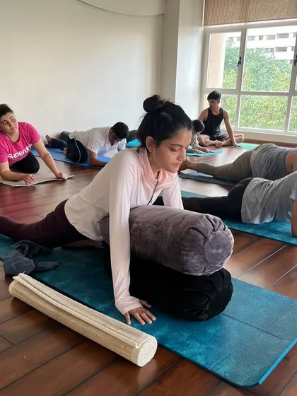 A student uses multiple bolsters to ease into a deep hip-opening stretch, allowing for a longer, more restorative hold.