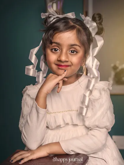 A girl with her hair in ribboned buns, dressed in a white vintage-style dress. This portrait has a classic, nostalgic charm.