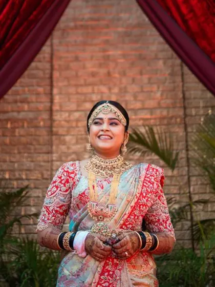 A joyful smile from the bride on her special day. Her custom-designed red blouse with detailed embroidery adds a vibrant touch to her elegant wedding saree.