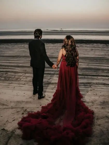 Another angle of the beach photoshoot, showing the full length of the dramatic red trail gown as the couple walks along the shore.