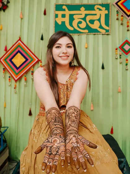 A happy bride in a vibrant mehendi ceremony setting, showcasing her full bridal henna.