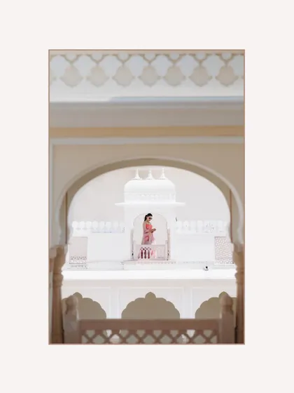 An artistic shot of a bride standing on a palace balcony, viewed through an archway, creating a sense of depth and grandeur.