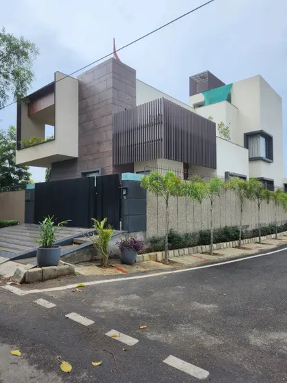 The exterior of a completed modern villa, showcasing a dynamic composition of different materials and forms. The design balances solid masses with open balconies and slatted screens to create a resort-like feel in a city environment.
