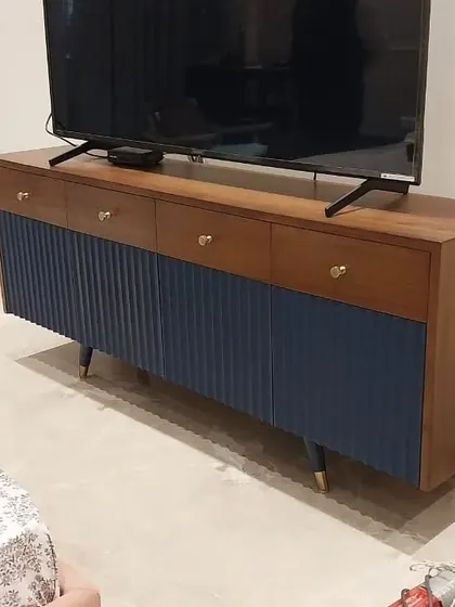 A two-tone media console with natural wood drawers and a navy blue fluted base. This piece combines practical TV storage with a mid-century modern aesthetic, featuring brass knobs and tapered legs.