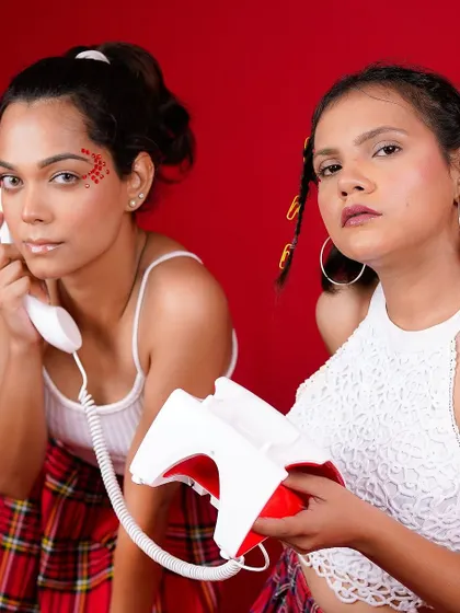 A fun and quirky editorial shot with two models and a vintage telephone against a bold red background. The playful styling and concept create a memorable and engaging fashion image.