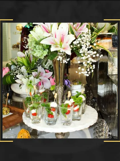 A beautiful display of caprese salad skewers in individual shot glasses, presented on a marble platter amidst a stunning floral arrangement.
