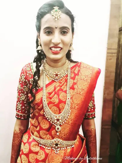 A phone-clicked photo showing the real, unedited makeup for a bride's reception. She is wearing a red silk saree with beautiful stone-work jewelry.