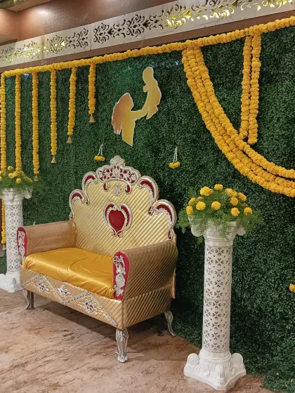 This is a classic setup for a Haldi or Mehendi ceremony. We used a full artificial green wall backdrop, decorated with traditional marigold flower garlands and a custom cutout, paired with a golden throne for the main seating.