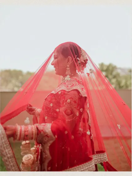 A side profile of the bride, her red veil gently obscuring her face for an artistic effect.