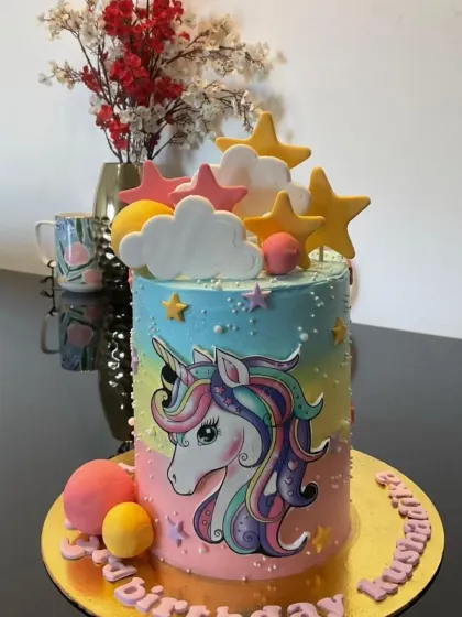 A colorful unicorn cake with a rainbow gradient. This design uses an edible print of a unicorn, surrounded by fondant stars and clouds.