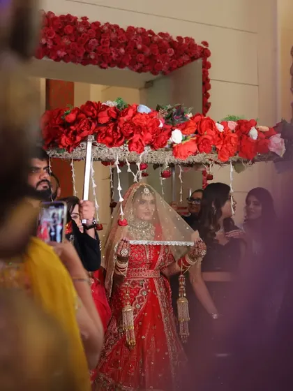 The bride makes her way to the stage under a beautiful floral 'phoolon ki chadar' held by her family, a cherished tradition.