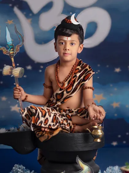 A young boy sits in a meditative pose as Lord Shiva, holding a trishul, with the Om symbol glowing behind him.
