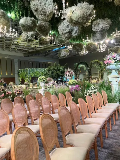 The guest seating area, with elegant wooden chairs arranged before the garden-like stage. The floating floral clouds above create a cohesive and immersive environment.