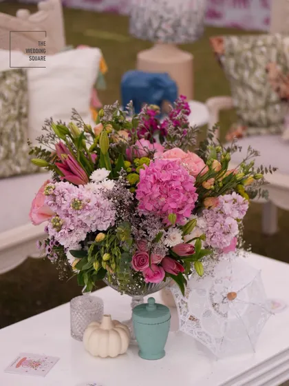 A beautiful centerpiece of pink hydrangeas and other pastel flowers, surrounded by whimsical decor items like a miniature lace umbrella.