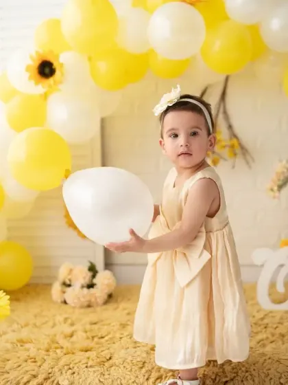 A full-length shot of the birthday girl in her pretty yellow dress, standing amidst a balloon arch. Our sets are designed to create a complete, festive scene.