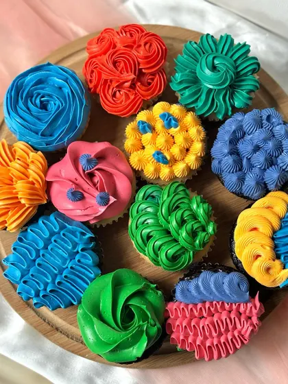 A vibrant set of cupcakes inspired by the movie 'Inside Out'. Each cupcake is frosted with brightly coloured buttercream using different piping styles to represent the emotions of Joy, Sadness, Anger, Fear, and Disgust.