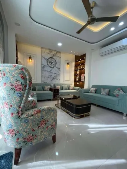 A complete view of a classic living room setup. The combination of a traditional floral wingback chair with modern sofas in a solid color adds character and creates a balanced, eclectic look.