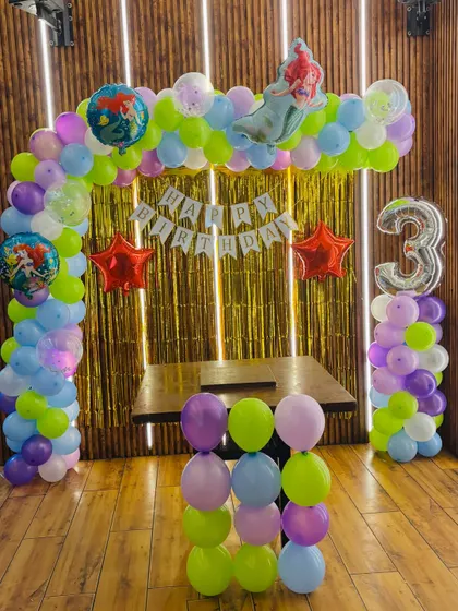 A magical mermaid-themed birthday party for a 3-year-old. The balloon arch uses pastel colors, and features Ariel and other sea-themed foil balloons.