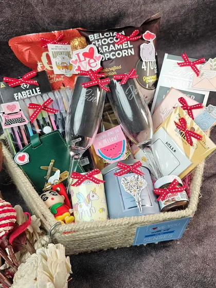 A beautiful couple's hamper in a jute basket. It's filled with personalized champagne glasses, gourmet popcorn, a custom passport cover, and other goodies for them to enjoy together.