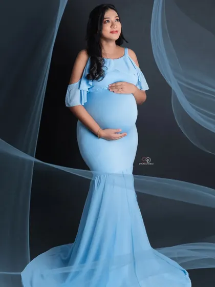 A classic maternity pose in a beautiful baby blue gown. The flowing fabric adds a sense of movement and grace to this elegant studio portrait against a simple black background.
