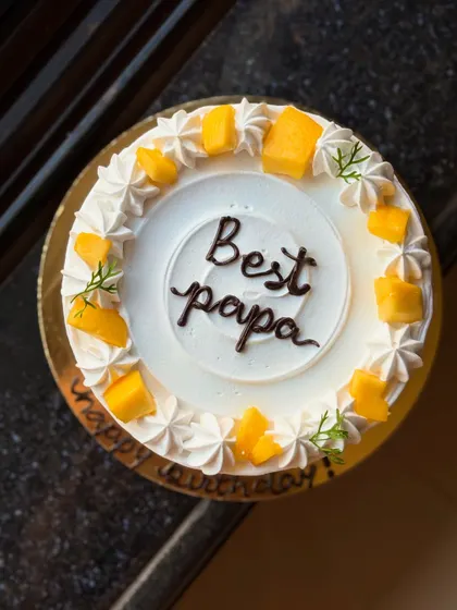 A closer look at the "Best Papa" mango cake, showing the fresh mango pieces and delicate green sprigs.