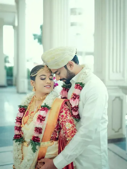 A romantic portrait of a couple in white wedding attire, sharing a quiet embrace in a beautiful, light-filled corridor.