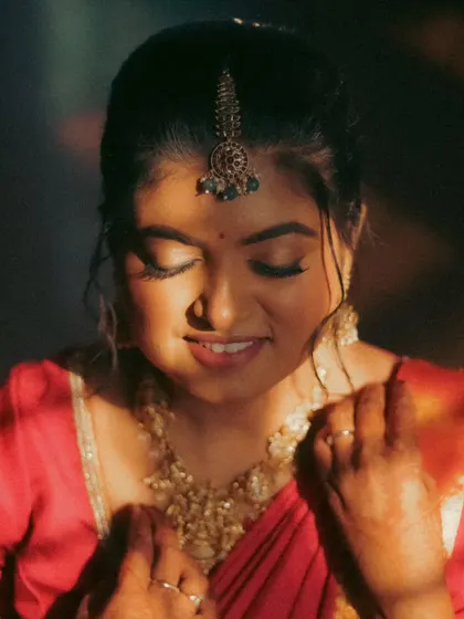 A close-up of a bride with her eyes closed, a soft smile on her face. The warm, directional light highlights her makeup and jewelry, creating a peaceful and beautiful portrait.