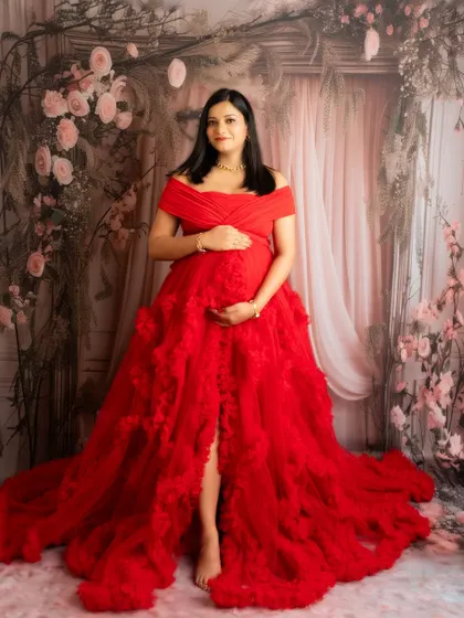 A classic standing portrait in a red ruffled gown against a romantic floral backdrop. The pose is confident and beautiful.
